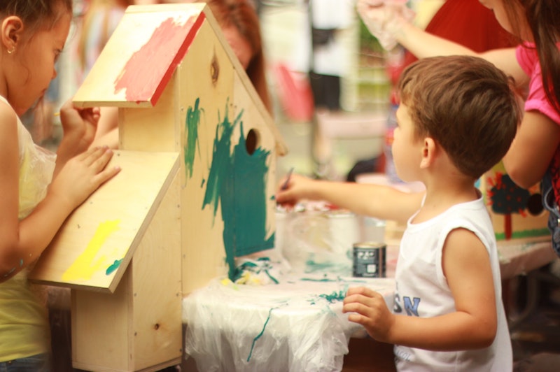 Kleiner Junge malt in der Kita ein Vogelhaus grün an.